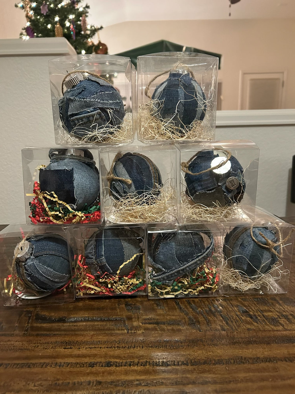 Stack of blue decorative ornaments in clear packaging on a wooden surface with a Christmas tree in the background.